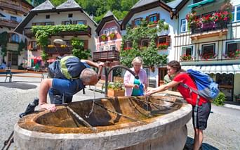 Groupe de randonneurs se rafraîchissant à une fontaine dans le village d'Hallstatt en Autriche