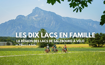 Trois cyclistes roulent sur un chemin à travers des prairies vertes avec des montagnes alpines spectaculaires en arrière-plan près de Salzbourg.