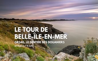 Côte rocheuse de Belle-Île-en-Mer avec falaises herbeuses surplombant une mer calme au coucher du soleil. Nuages roses et violets dans le ciel.