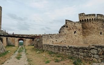 Forteresse historique de Belgrade avec murs en pierre, tour ronde et pont. Chemin traverse les fortifications sous ciel nuageux.