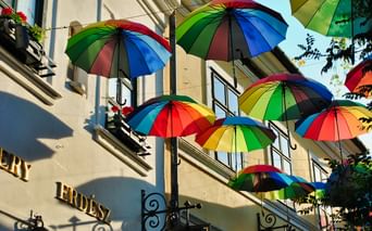 Parapluies arc-en-ciel suspendus au-dessus d'une rue à Szentendre, Hongrie. Façade de bâtiment avec fenêtres et jardinières visible en dessous.
