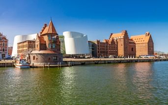 Ozeaneum Stralsund avec architecture moderne blanche courbée à côté de bâtiments historiques en brique au bord de l'eau.