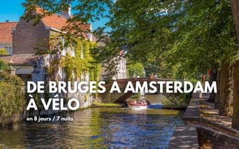 Canal pittoresque à Bruges avec bateaux, pont en pierre, chemin bordé d'arbres et bâtiments historiques aux façades couvertes de lierre.