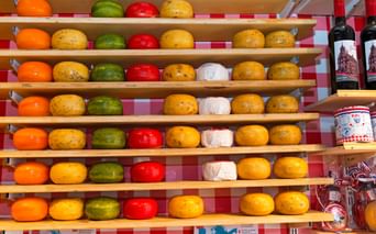 Étalage de meules de Gouda colorées sur étagères en bois à Gouda. Fromages enrobés de cire orange, jaune, verte, rouge et blanche.