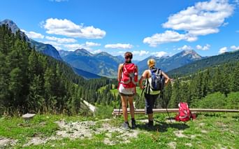Deux randonneuses avec sacs à dos debout à une barrière en bois surplombant vallée alpine près de la Zugspitze avec montagnes boisées.