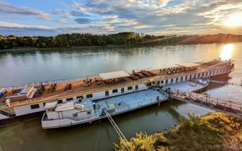 Bateau de croisière MS Princess Katharina amarré sur le Danube au coucher du soleil, avec la lumière dorée se reflétant sur l'eau et des collines boisées en arrière-plan.