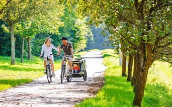 Couple de parent en ballade à vélo avec leur enfant dans une remorque