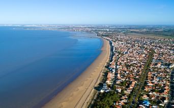 Vue aérienne de Châtelaillon-Plage montrant une longue plage de sable, l'océan bleu et la ville résidentielle aux toits rouges le long de la côte.