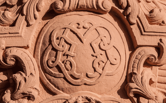 Blason sculpté en grès orné Blason en grès finement sculpté avec des éléments décoratifs baroques ornés et des volutes entourant un écu héraldique central.