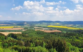 Vue panoramique de la campagne tchèque avec des champs, des forêts et des collines sous un ciel bleu avec des nuages blancs.