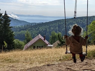 Petite fille se balançant sur une balançoire suspendue à un sapin devant un paysage de montagne vosgienne
