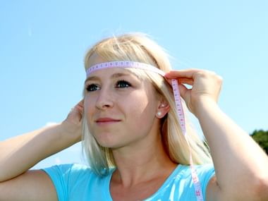 Jeune femme mesure son tour de tête à l'aide d'un mètre-ruban