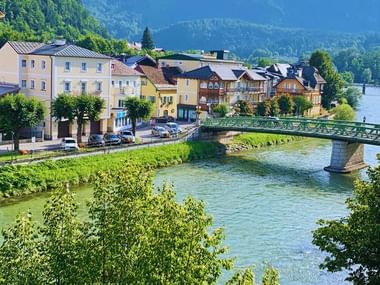 Vue pittoresque de Bad Ischl avec des bâtiments colorés le long d'une rivière, pont vert traversant l'eau, entouré de montagnes boisées.