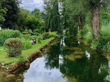 Ruisseau cristallin coulant à travers un parc paysager à Bad Goisern avec des arbres verts luxuriants, des pelouses entretenues et des reflets nuageux.