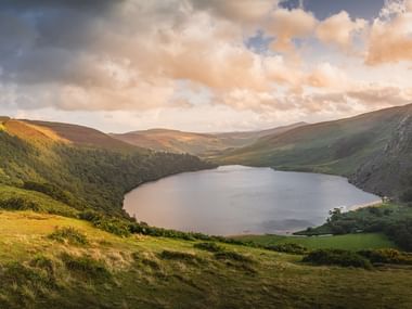Vue panoramique d'un lac calme niché entre des collines verdoyantes sur le Wicklow Way, Irlande, sous un ciel nuageux dramatique.