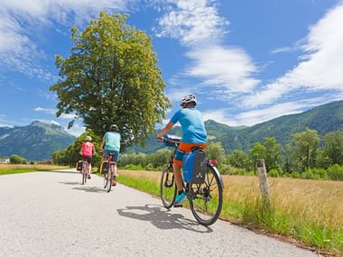 Petit groupe de cyclistes pédalant de dos sur une piste cyclables, les montagnes du Salzkammergut en toile de fond