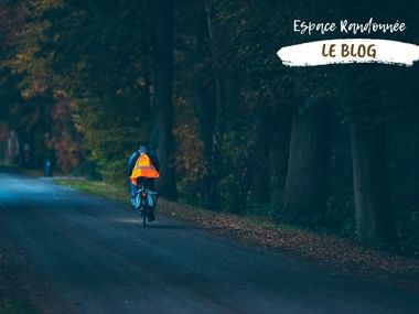 Cycliste de dos, portant un gilet réfléchissant de nuit sur une route non éclairée