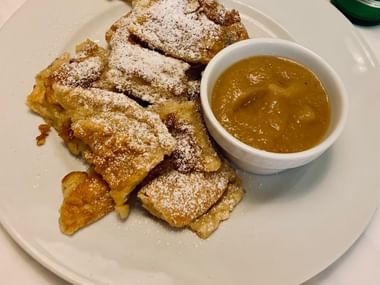 Dessert autrichien traditionnel Kaiserschmarrn sur assiette blanche, morceaux de crêpe déchirés saupoudrés de sucre glace, servi avec confiture.