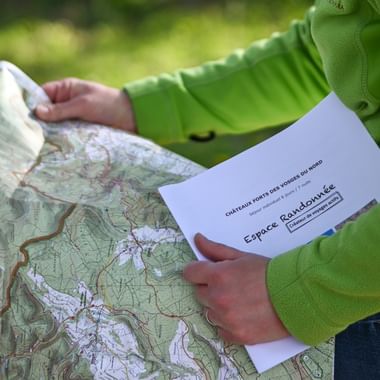 Randonneuse lisant une carte IGN et tenant un topoguide du circuit Vosges du Nord d'Espace Randonnée