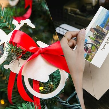 Mains tenant un bon cadeau voyage Espace Randonnée avec images de randonnée, décoré d'un nœud rouge et branche de sapin près du sapin de Noël.