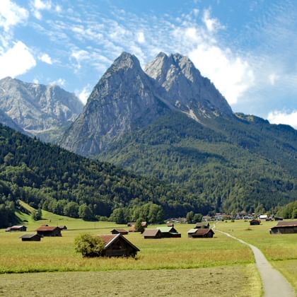 Vue panoramique sur la Zugspitze avec des pics rocheux spectaculaires dominant une vallée alpine verte parsemée de chalets en bois.
