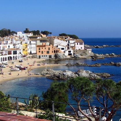 Vue panoramique du village balnéaire de Calella sur la Costa Brava avec bâtiments blancs, plage de sable, côte rocheuse et mer Méditerranée.