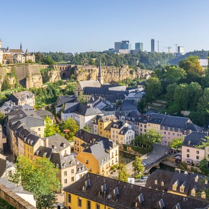Vue panoramique de Luxembourg-Ville montrant des bâtiments historiques colorés dans la vallée, des murs de fortification anciens et une skyline moderne.