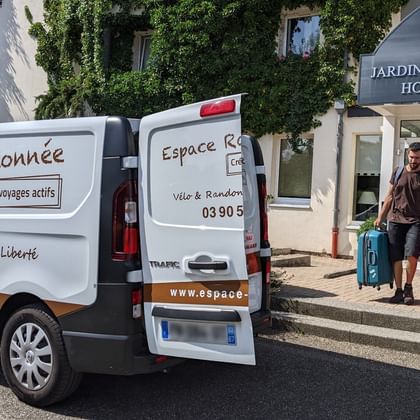 Un membre de l'équipe d'Espace Randonnée transportant les bagages de clients devant un hôtel à Obernai