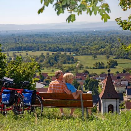 Couple de cyclotouristes profitent d'une pause détente sur un banc surplombant un vignoble de la Forêt-Noire du Sud
