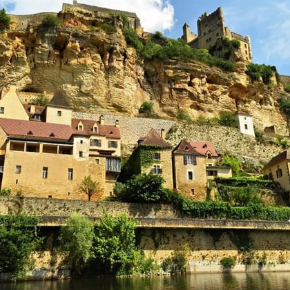 Maisons en pierre aux toits de tuiles construites le long d'une falaise calcaire spectaculaire en Périgord Noir, avec ruines de château en haut.