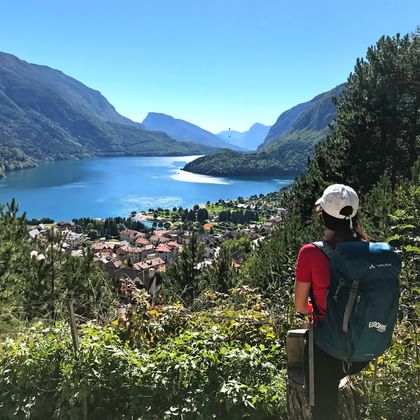 Randonneur avec sac à dos et casquette admirant le lac de Molveno depuis un point de vue élevé, avec montagnes et village au bord du lac bleu.