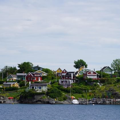 Petite île norvégienne avec maisons en bois colorées sur une colline surplombant un fjord. Bateaux amarrés aux quais, entourés de végétation.