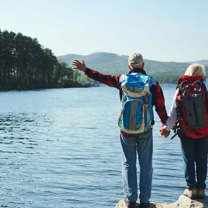 couple de randonneurs qui se tiennent la main de dos en observant devant eux un lac et ses sapins