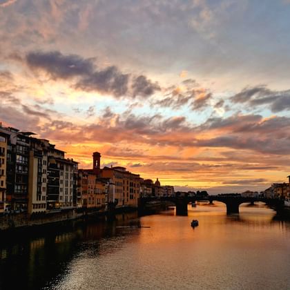Coucher de soleil spectaculaire sur l'Arno à Florence avec des nuages colorés, des bâtiments historiques bordant les rives et un pont.