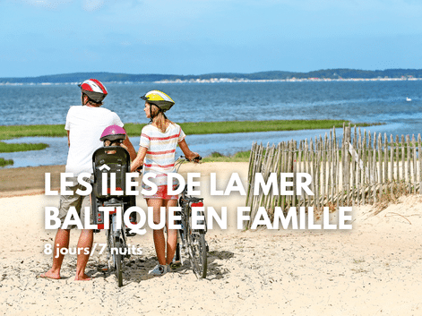Famille avec vélos sur plage sablonneuse de la mer Baltique. Deux adultes et enfant avec casques près d'une clôture en bois, eau bleue visible.