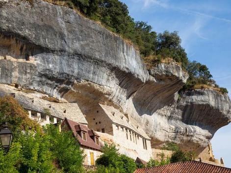 Maisons en pierre historiques construites dans une falaise calcaire massive aux Eyzies. Les bâtiments présentent une architecture traditionnelle.