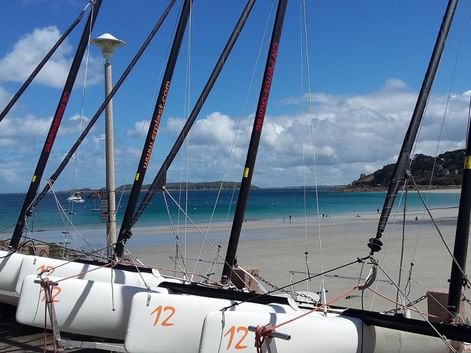 Voiliers blancs numérotés 12 sur la plage de sable de Perros-Guirec avec eau turquoise, ciel bleu avec nuages blancs et côte rocheuse.
