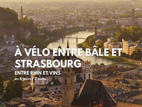 Vue aérienne de Bâle avec le Rhin, des ponts et des clochers à l'heure dorée. Texte: circuit à vélo entre Bâle et Strasbourg.