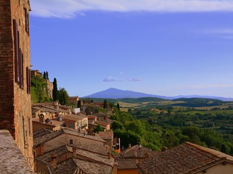 Vue de Montepulciano montrant des toits en terre cuite, des cyprès et des collines toscanes avec une montagne lointaine sous un ciel bleu.