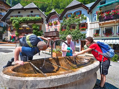 Groupe de randonneurs se rafraîchissant à une fontaine dans le village d'Hallstatt en Autriche