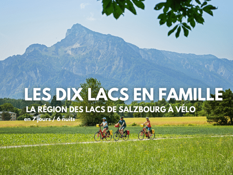 Trois cyclistes roulent sur un chemin à travers des prairies vertes avec des montagnes alpines spectaculaires en arrière-plan près de Salzbourg.
