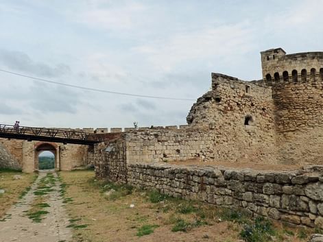 Forteresse historique de Belgrade avec murs en pierre, tour ronde et pont. Chemin traverse les fortifications sous ciel nuageux.