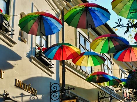 Parapluies arc-en-ciel suspendus au-dessus d'une rue à Szentendre, Hongrie. Façade de bâtiment avec fenêtres et jardinières visible en dessous.