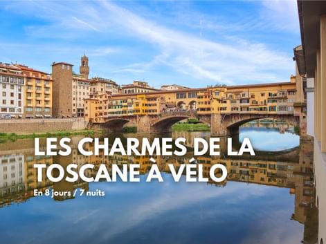 Pont Ponte Vecchio avec bâtiments historiques enjambant l'Arno à Florence. Bâtiments jaunes et oranges se reflétant dans l'eau calme sous ciel bleu.
