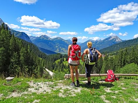 Deux randonneuses avec sacs à dos debout à une barrière en bois surplombant vallée alpine près de la Zugspitze avec montagnes boisées.