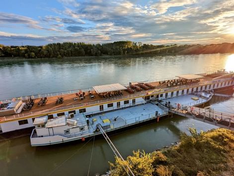 Bateau de croisière MS Princess Katharina amarré sur le Danube au coucher du soleil, avec la lumière dorée se reflétant sur l'eau et des collines boisées en arrière-plan.