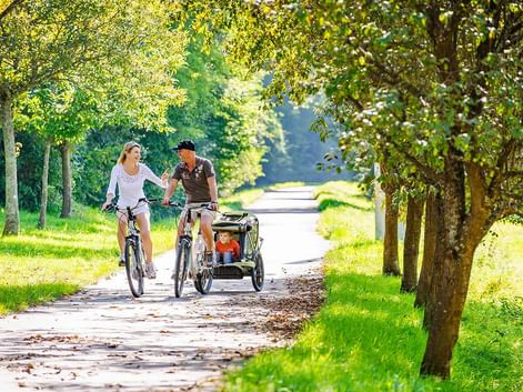 Couple de parent en ballade à vélo avec leur enfant dans une remorque