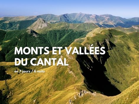 Vue aérienne des montagnes volcaniques vertes et vallées du Cantal depuis le Puy Mary, montrant des collines sous un ciel bleu.