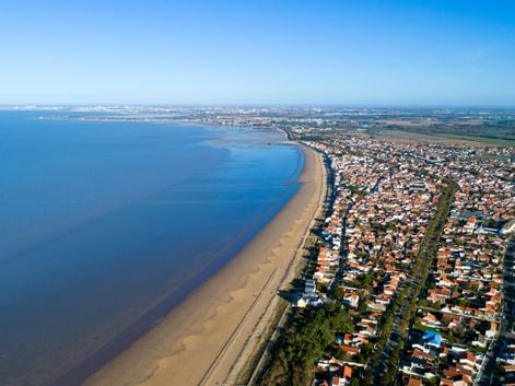 Vue aérienne de Châtelaillon-Plage montrant une longue plage de sable, l'océan bleu et la ville résidentielle aux toits rouges le long de la côte.