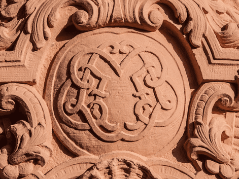 Blason sculpté en grès orné Blason en grès finement sculpté avec des éléments décoratifs baroques ornés et des volutes entourant un écu héraldique central.